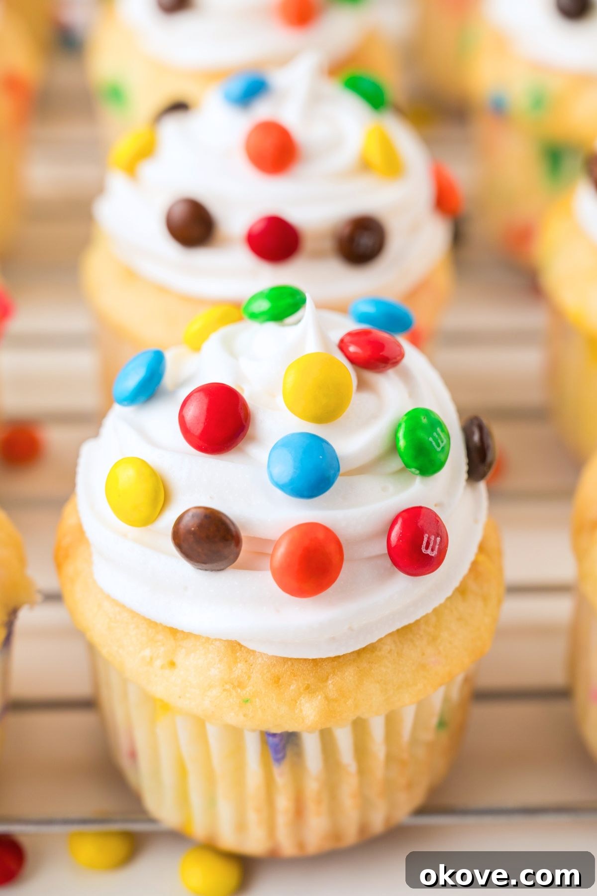 A vibrant display of funfetti M&M cupcakes, filled with candies and generously topped with smooth vanilla frosting and more colorful M&Ms, ready to be enjoyed.