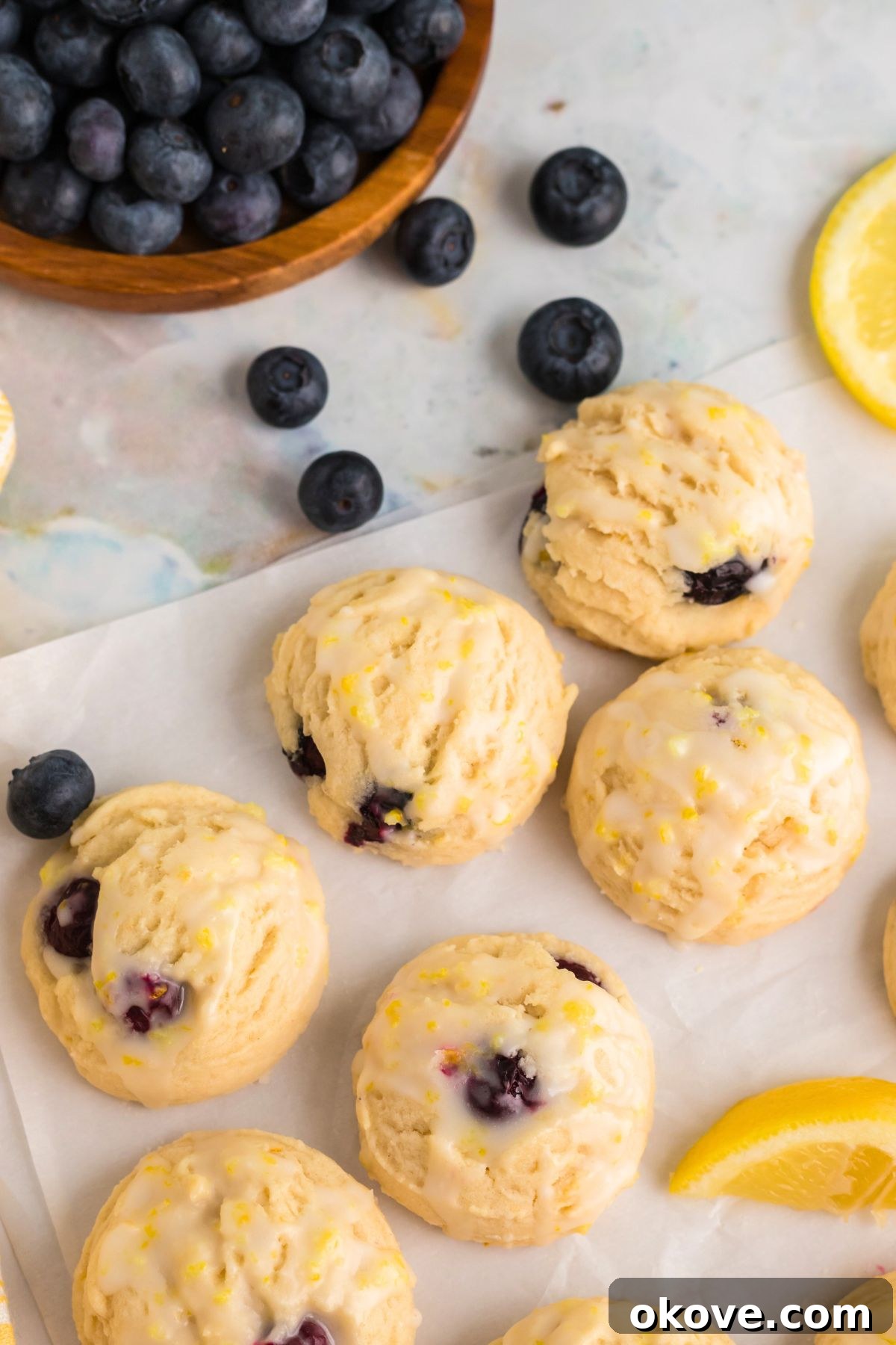 Tangy Blueberry Lemon Delights 2 Freshly baked lemon blueberry cookies arranged on parchment paper, adorned with vibrant lemon wedges and scattered blueberries.