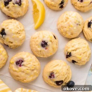 Lemon blueberry cookies on parchment paper with lemon wedges and blueberries scattered next to them.