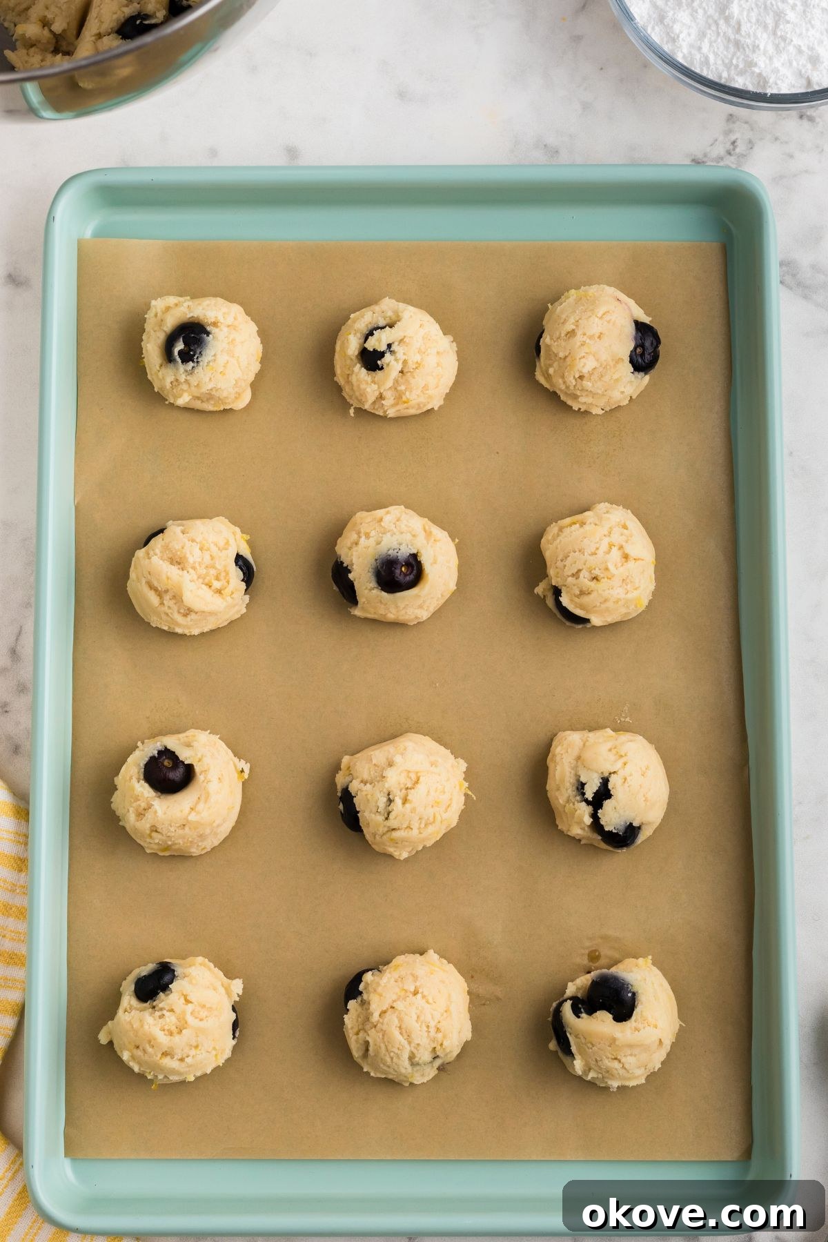 Tangy Blueberry Lemon Delights 8 Evenly portioned cookie dough balls, measured with a scoop, neatly arranged on a parchment-lined baking sheet, ready to go into the oven.