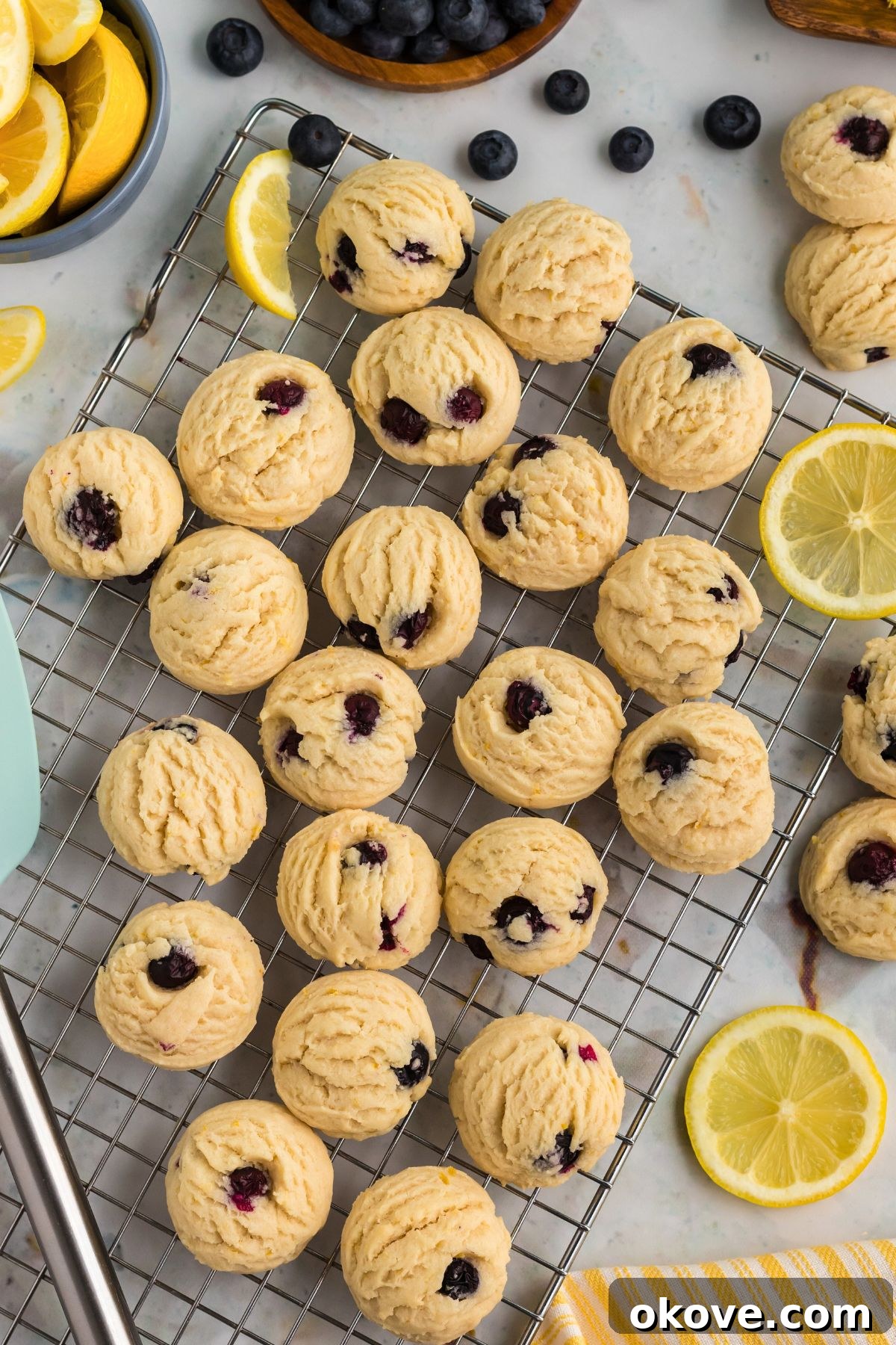 Tangy Blueberry Lemon Delights 10 Glazed lemon blueberry cookies neatly arranged on a wire cooling rack, surrounded by fresh blueberries and lemon wedges, highlighting their vibrant appeal.