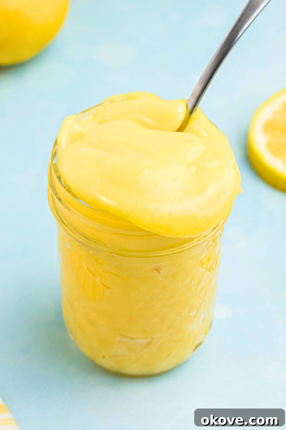 Zesty Lemon Delight 2 Bright yellow lemon curd in a small jar with a spoon being scooped out, showcasing its smooth and creamy texture.