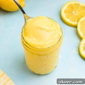 Bright yellow lemon curd in a small jar with a spoon being scooped out, indicating its rich and smooth texture.