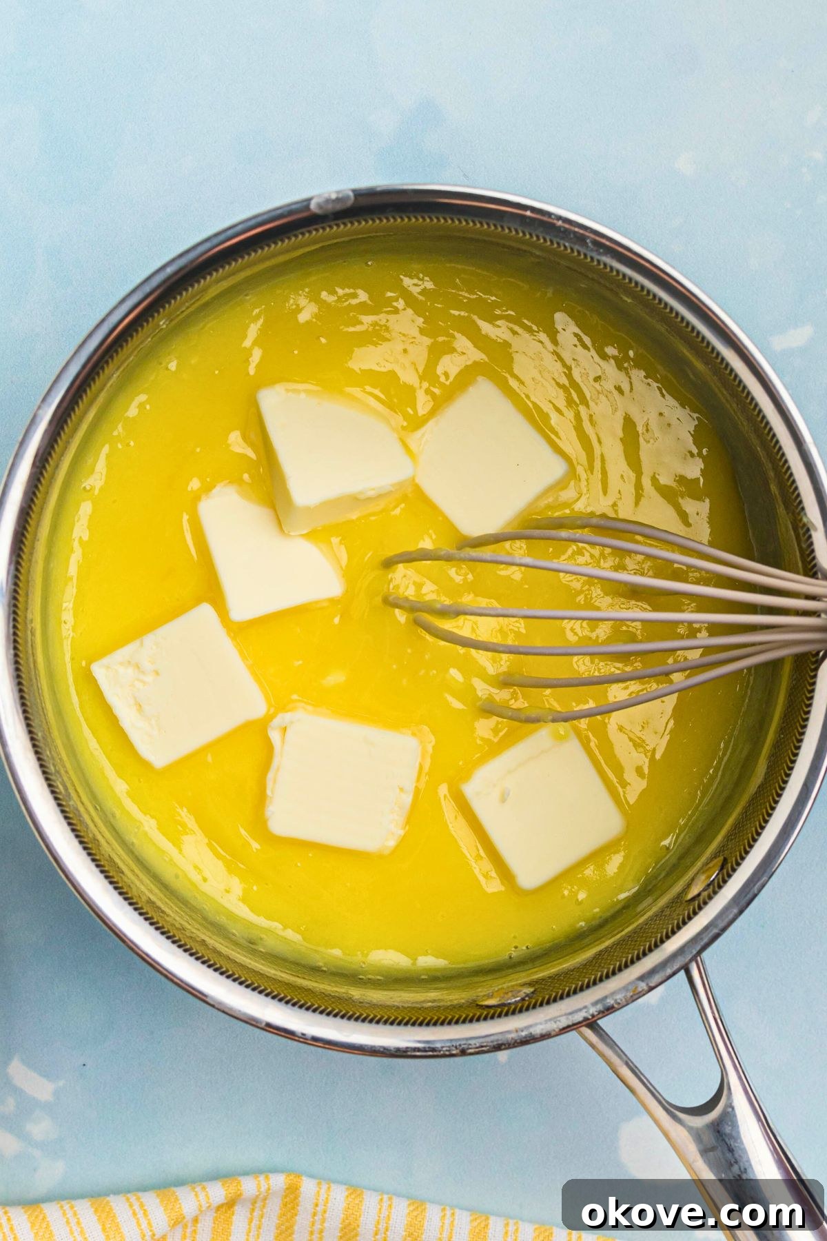 Zesty Lemon Delight 5 Small pieces of unsalted butter being stirred into the hot lemon curd mixture in a saucepan, melting to create a smooth texture.