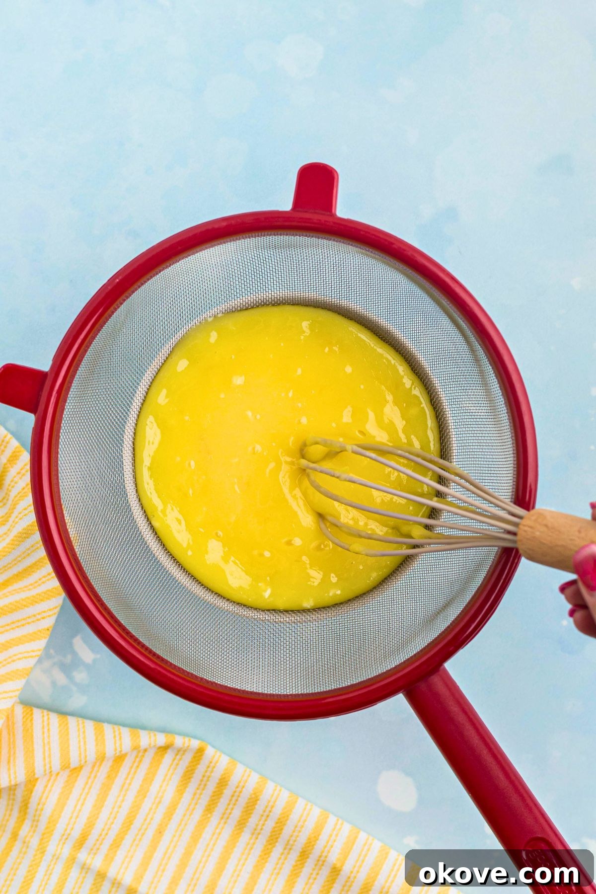 Zesty Lemon Delight 6 Hot lemon curd being strained through a fine mesh sieve into a clean bowl, ensuring a perfectly smooth and creamy texture by removing any solids.