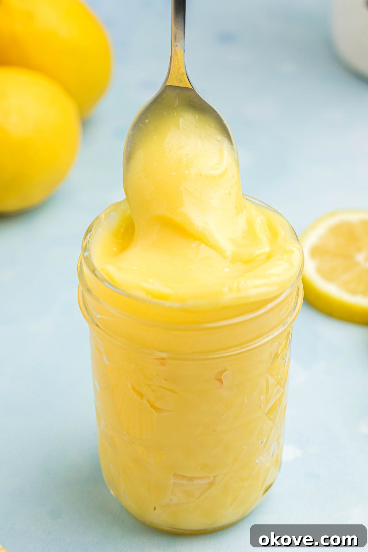 Zesty Lemon Delight 7 Bright yellow lemon curd in a small jar with a spoon being scooped out, highlighting its vibrant color and luscious texture.