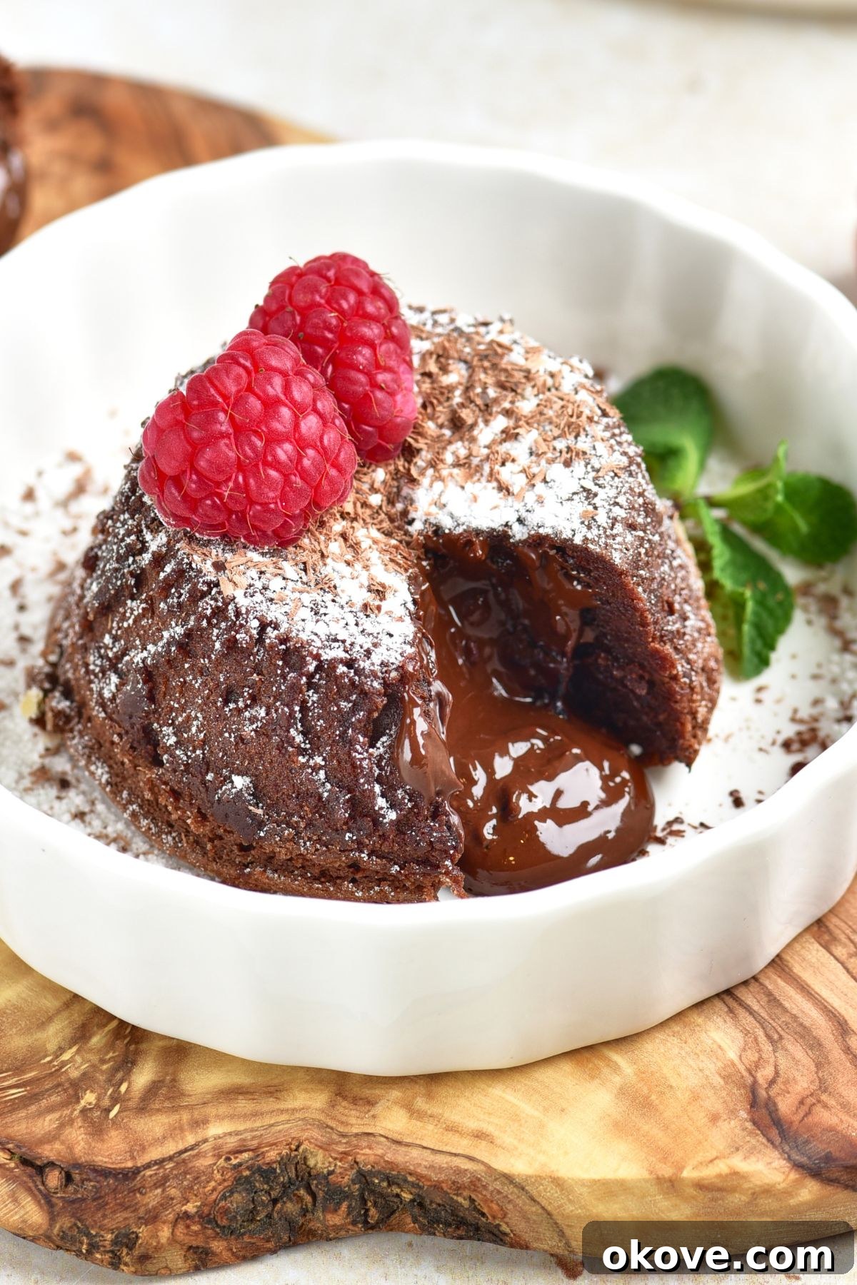 Molten Chocolate Dream 2 A mini chocolate cake with a gooey, molten chocolate center spilling out onto a pristine white plate, garnished with a single fresh raspberry.