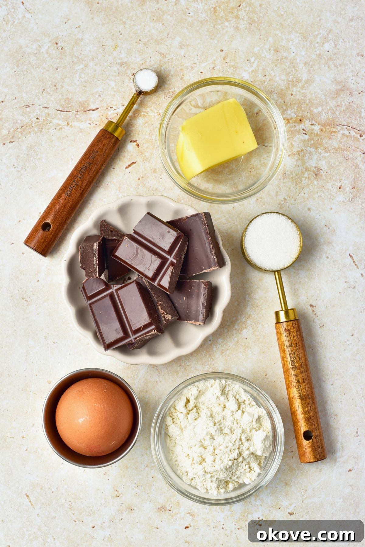Molten Chocolate Dream 3 Various ingredients like unsalted butter, dark chocolate, eggs, sugar, and flour measured into small glass bowls, arranged neatly on a marble countertop, ready for baking.