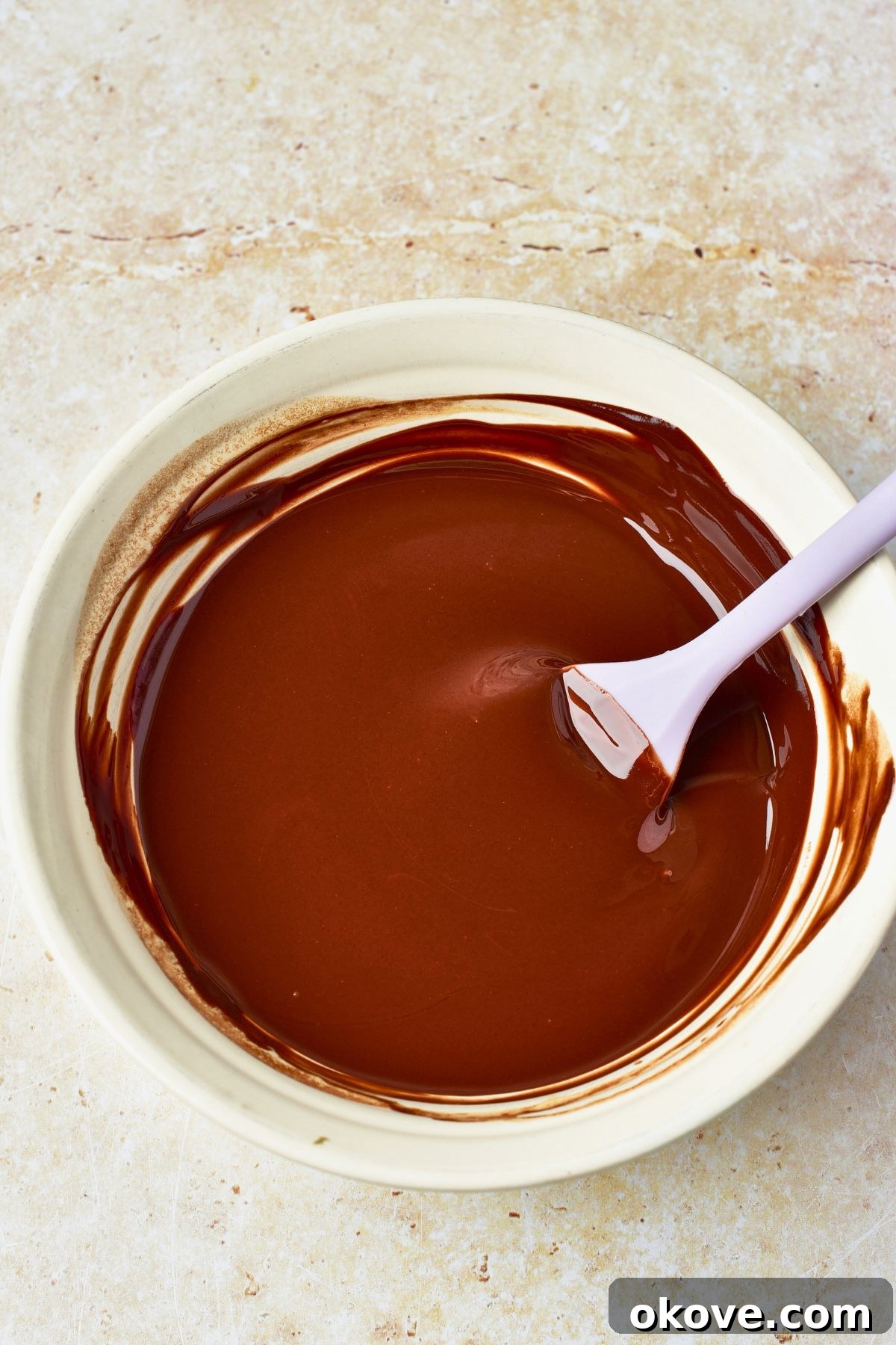 Molten Chocolate Dream 4 Smooth, glossy melted chocolate and butter mixture in a white ceramic bowl, with a spoon resting inside.
