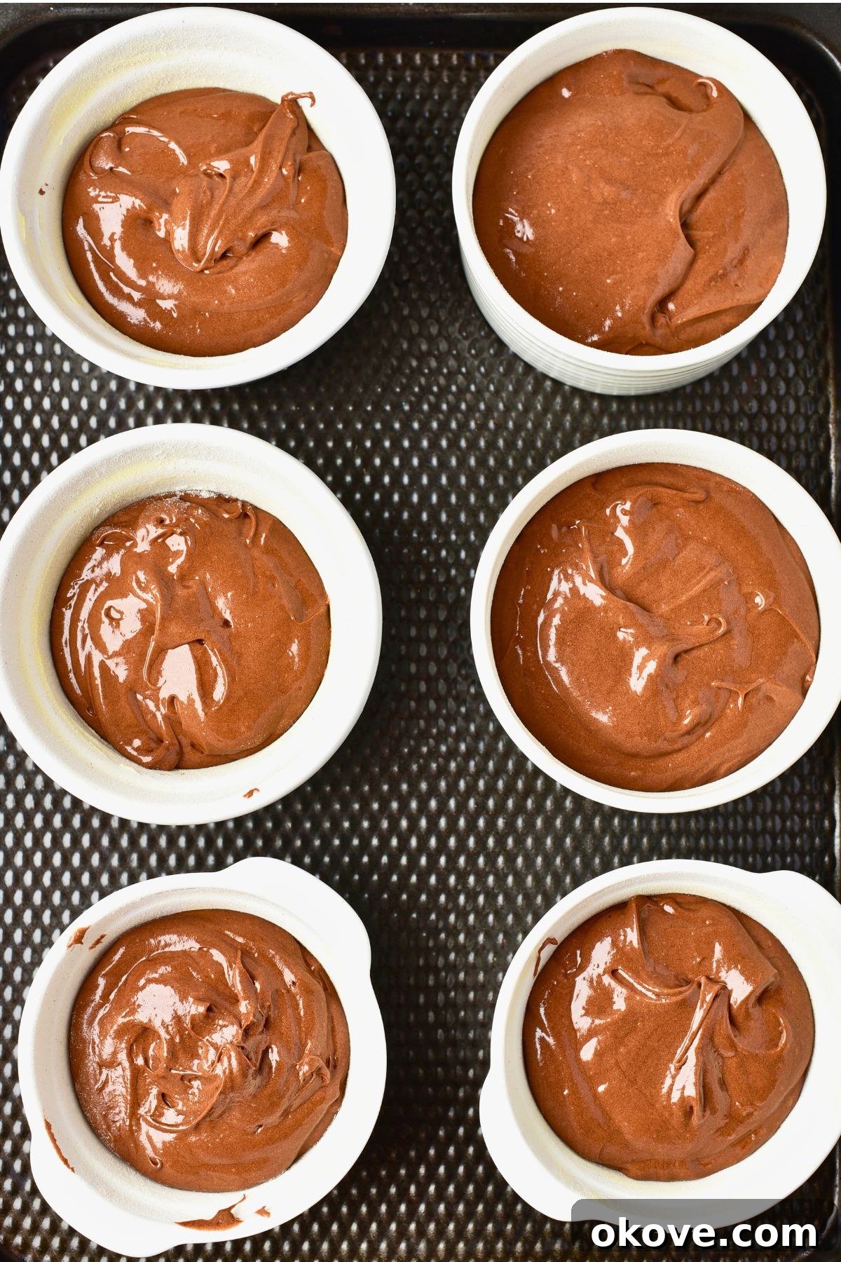 Molten Chocolate Dream 7 Six ramekins filled with smooth chocolate cake batter, neatly arranged on a baking sheet, ready to be placed in the oven.