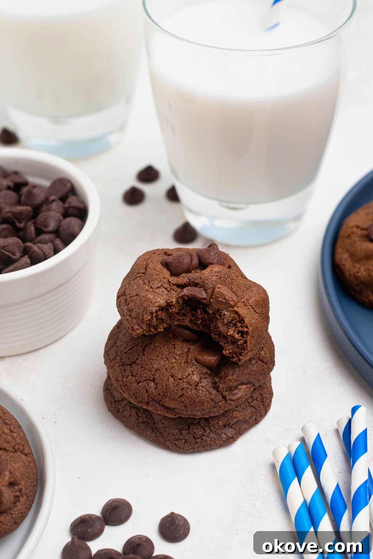 Luscious Double Chocolate Chip Cookies 8 Stack of warm double chocolate chip cookies on a marble table, with a glass of milk in the background.