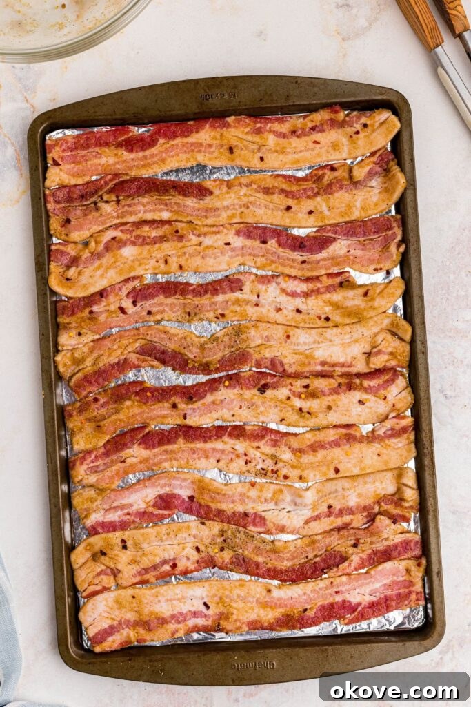 Decadent Caramelized Bacon 5 Uncooked bacon that has been coated with sugar and spices on a baking sheet lined with foil.