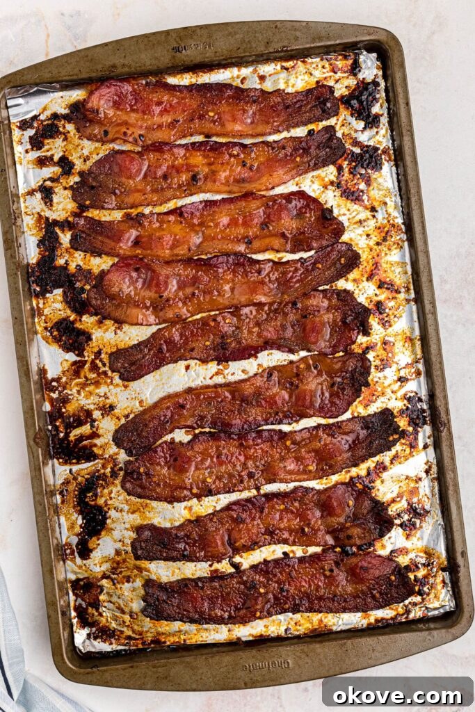 Decadent Caramelized Bacon 6 Golden juicy bacon slices on a baking sheet after cooking in the oven.