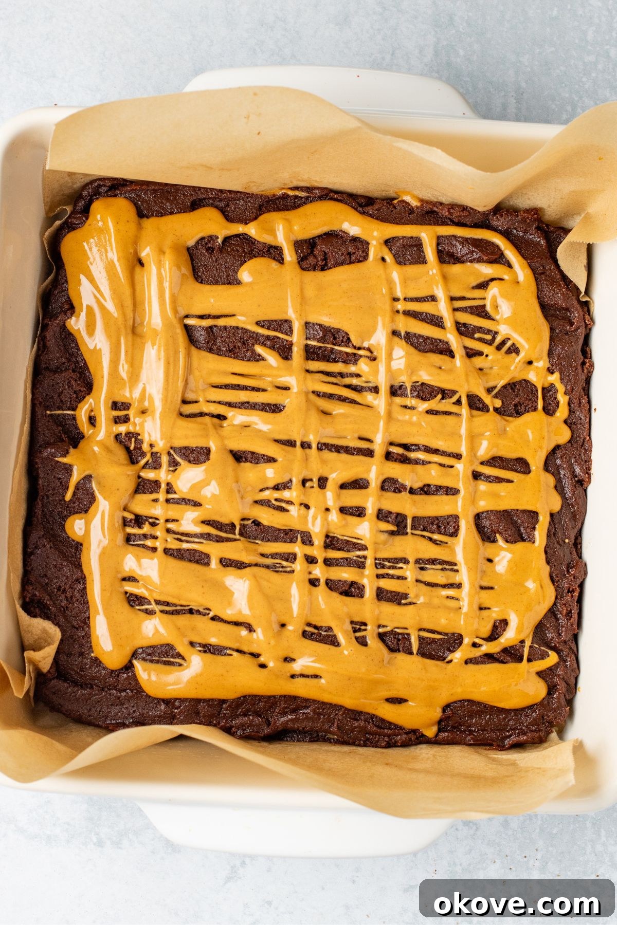 Chocolate brownie batter, topped with peanut butter filling in an 8x8 baking dish.