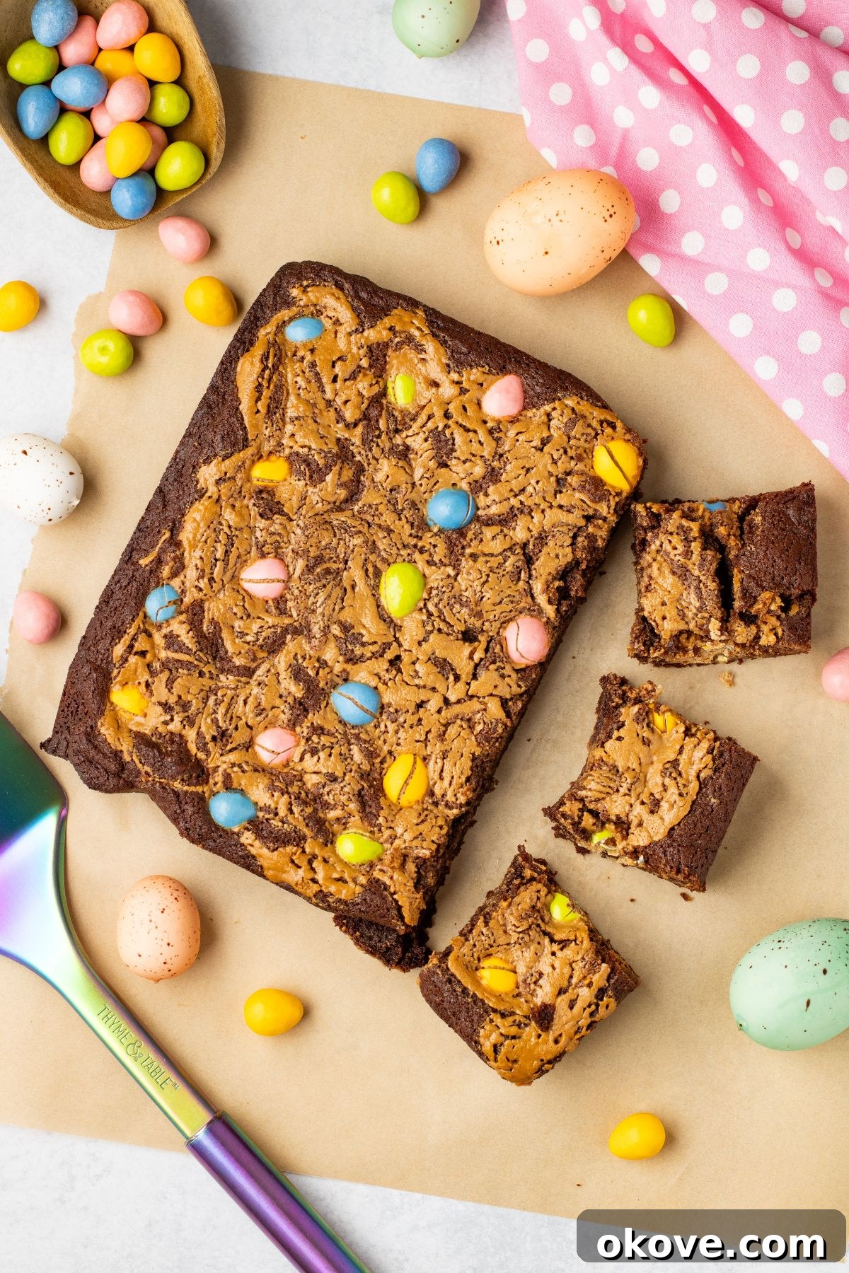 Easter brownies being cut into squares with candies on the table along with a pink linen.