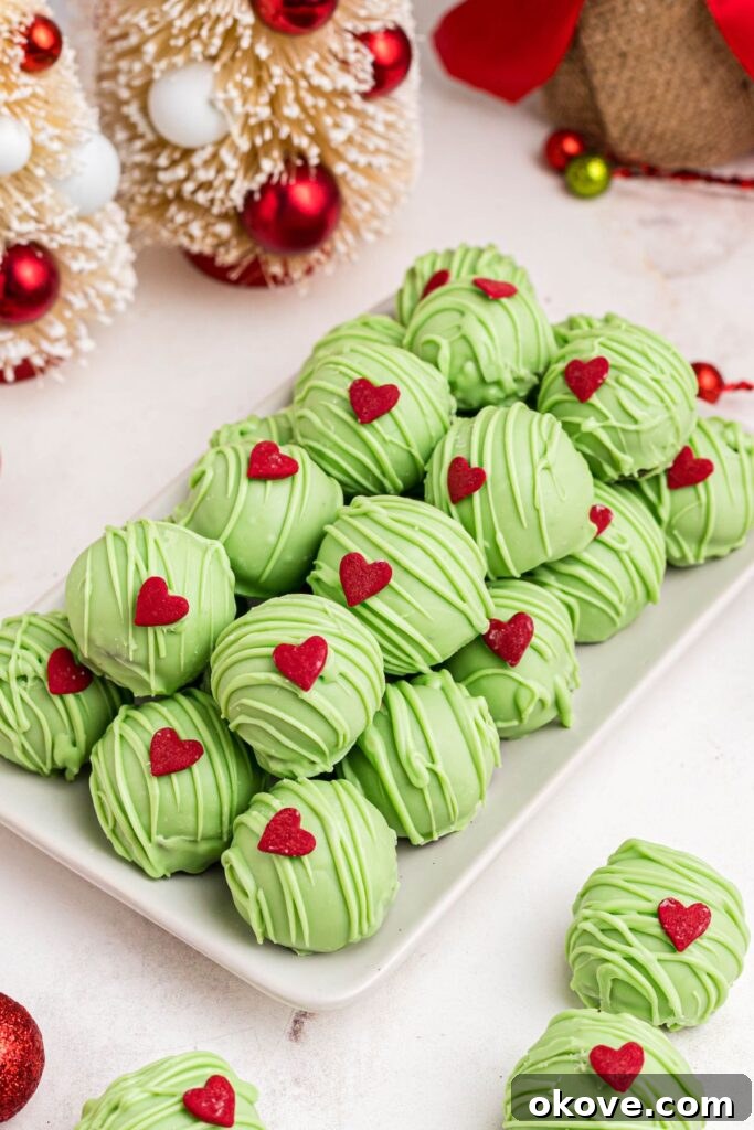 Green Grinch Oreo balls stacked on a white plate, adorned with tiny red heart sprinkles.