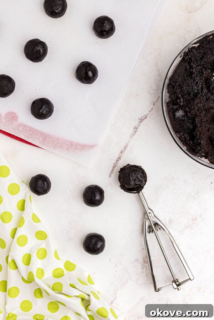 Scoops of Oreo and cream cheese mixture, expertly rolled into uniform balls, laid out on parchment paper on a baking sheet.