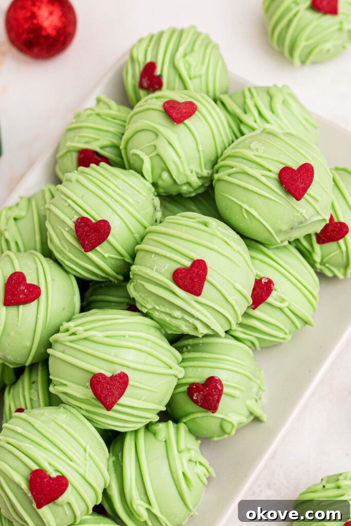 A close-up of a perfectly formed Grinch Oreo ball with a vibrant green coating and a distinct red heart sprinkle on top.