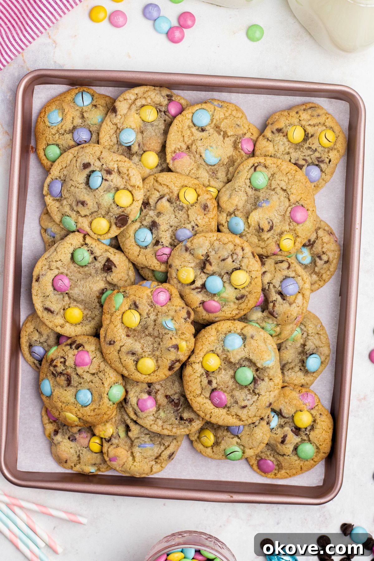Golden chocolate chip cookies with pastel candies on a pink baking sheet lined with parchment paper.