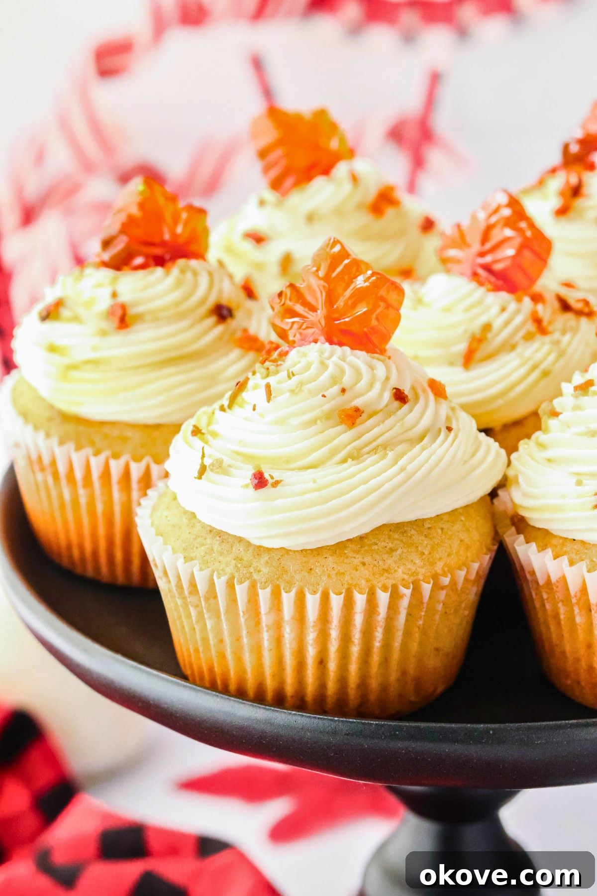 Golden maple bacon cupcakes arranged beautifully on a sleek black stand, adorned with delicate crumbles of crispy bacon on top.