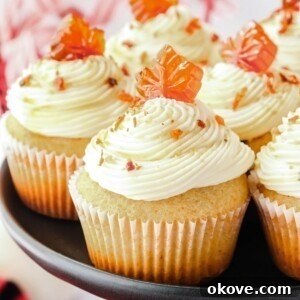Beautifully frosted maple bacon cupcakes on a black stand with crumbled bacon sprinkled on top.