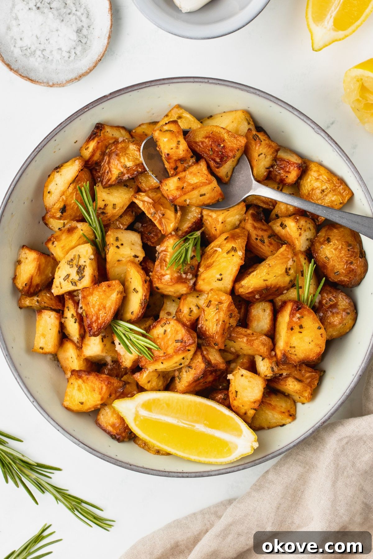 The Ultimate Roasted Spuds 2 Golden crispy roasted potatoes in a white serving bowl, with a spoon lifting a serving.