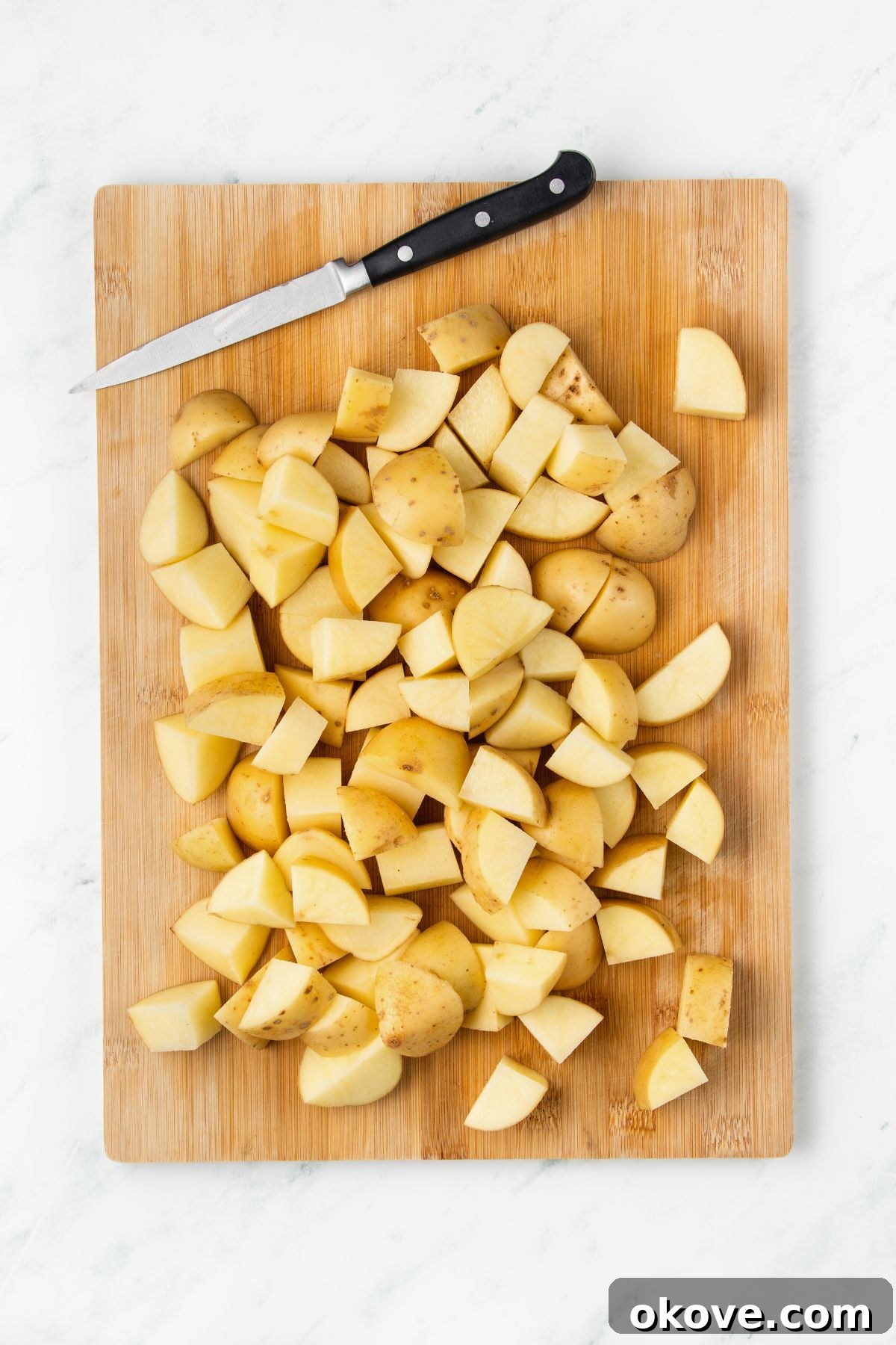 The Ultimate Roasted Spuds 4 Potatoes cut into uniform bite-sized pieces on a wooden cutting board.