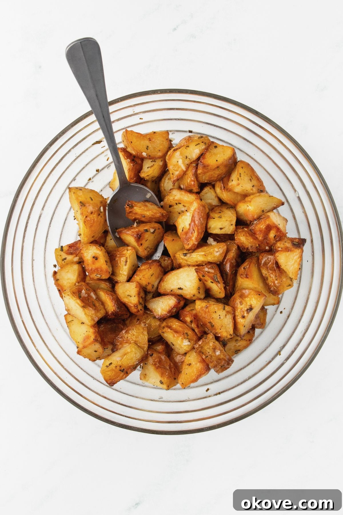 The Ultimate Roasted Spuds 7 Roasted potato pieces being tossed with a lemon garlic mixture in a large bowl.