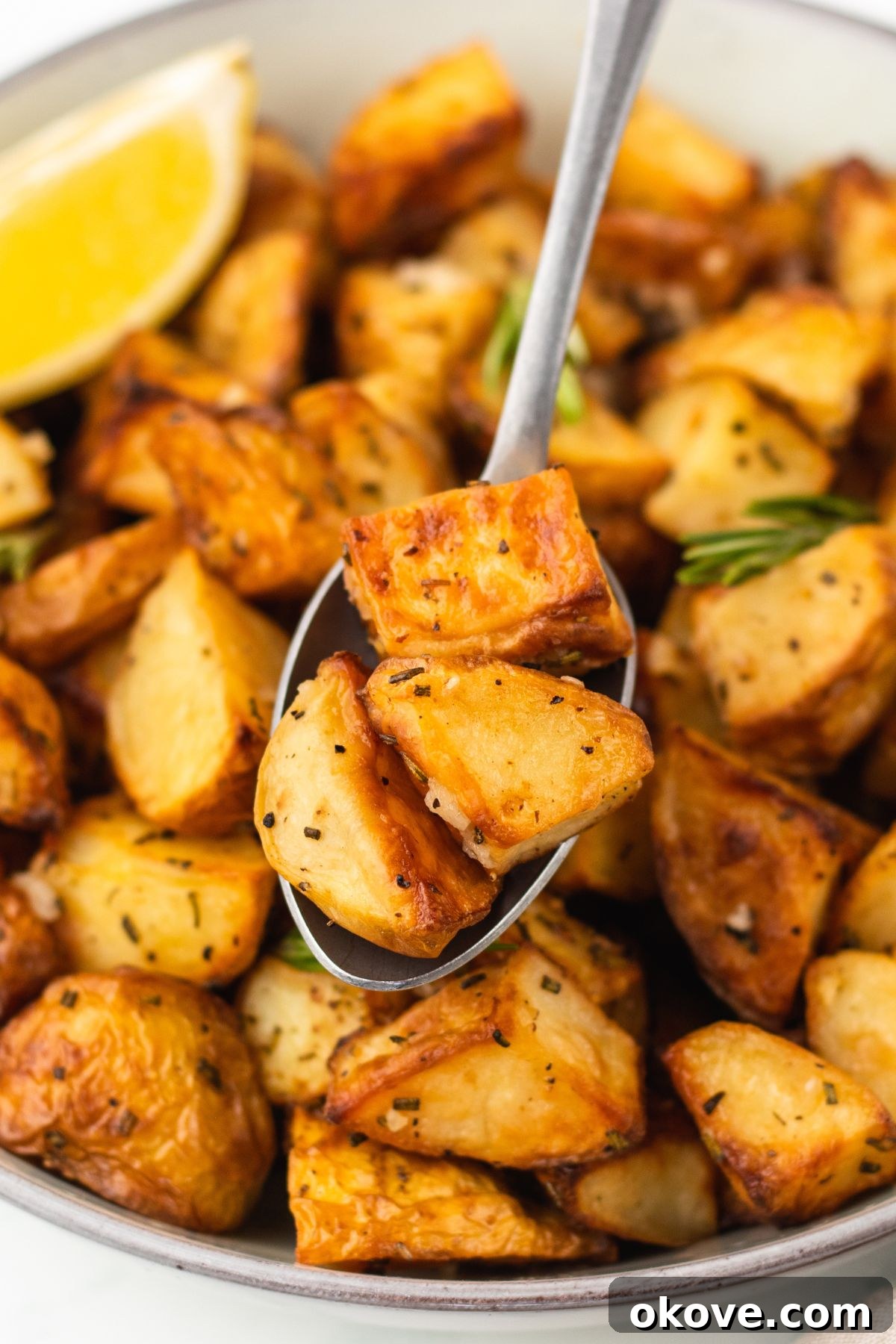 The Ultimate Roasted Spuds 8 Easy garlic roasted potatoes served in a white bowl, with a serving spoon.