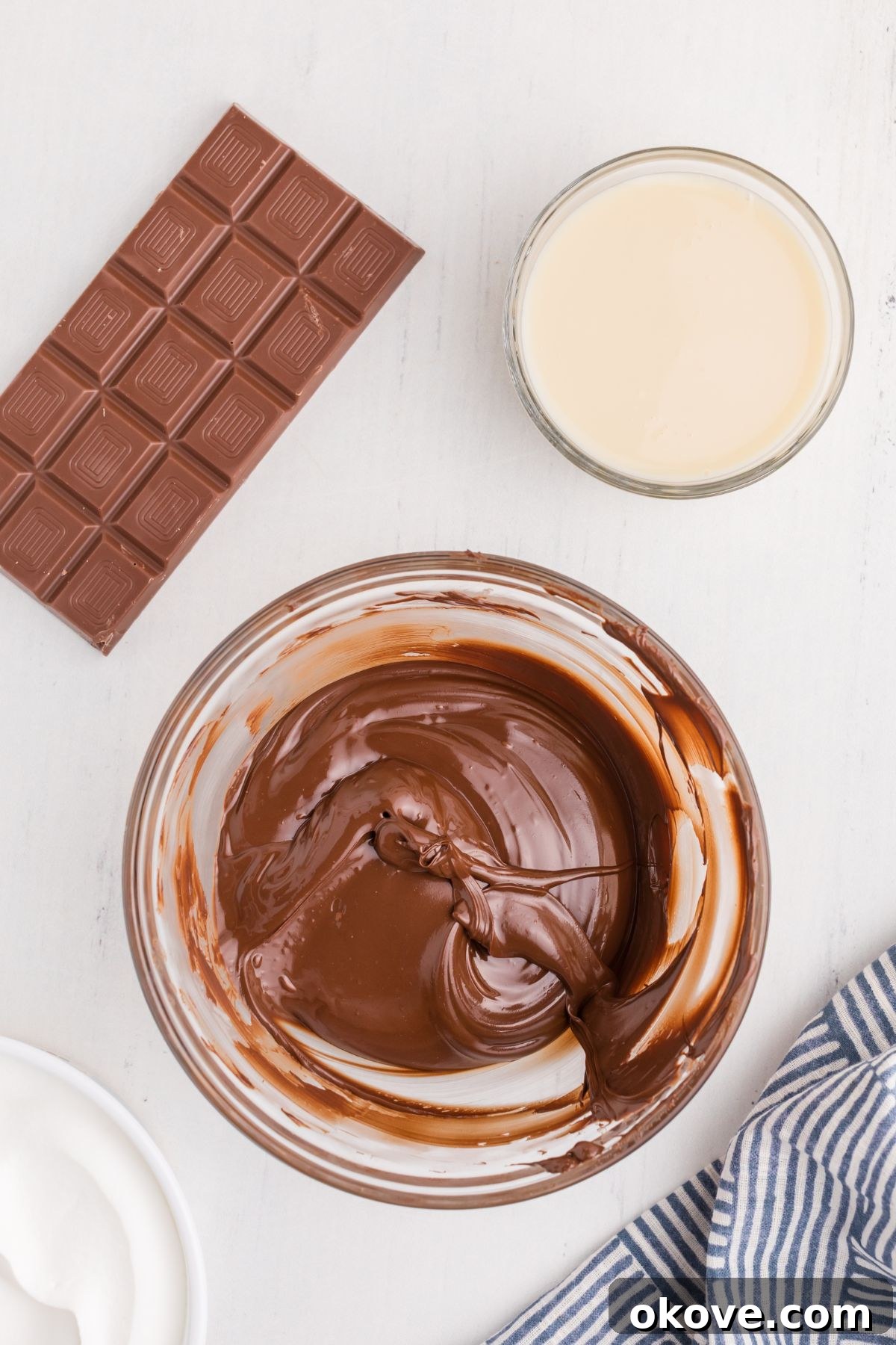A small, clear glass bowl containing perfectly melted chocolate, smooth and glossy, set against a bright background.