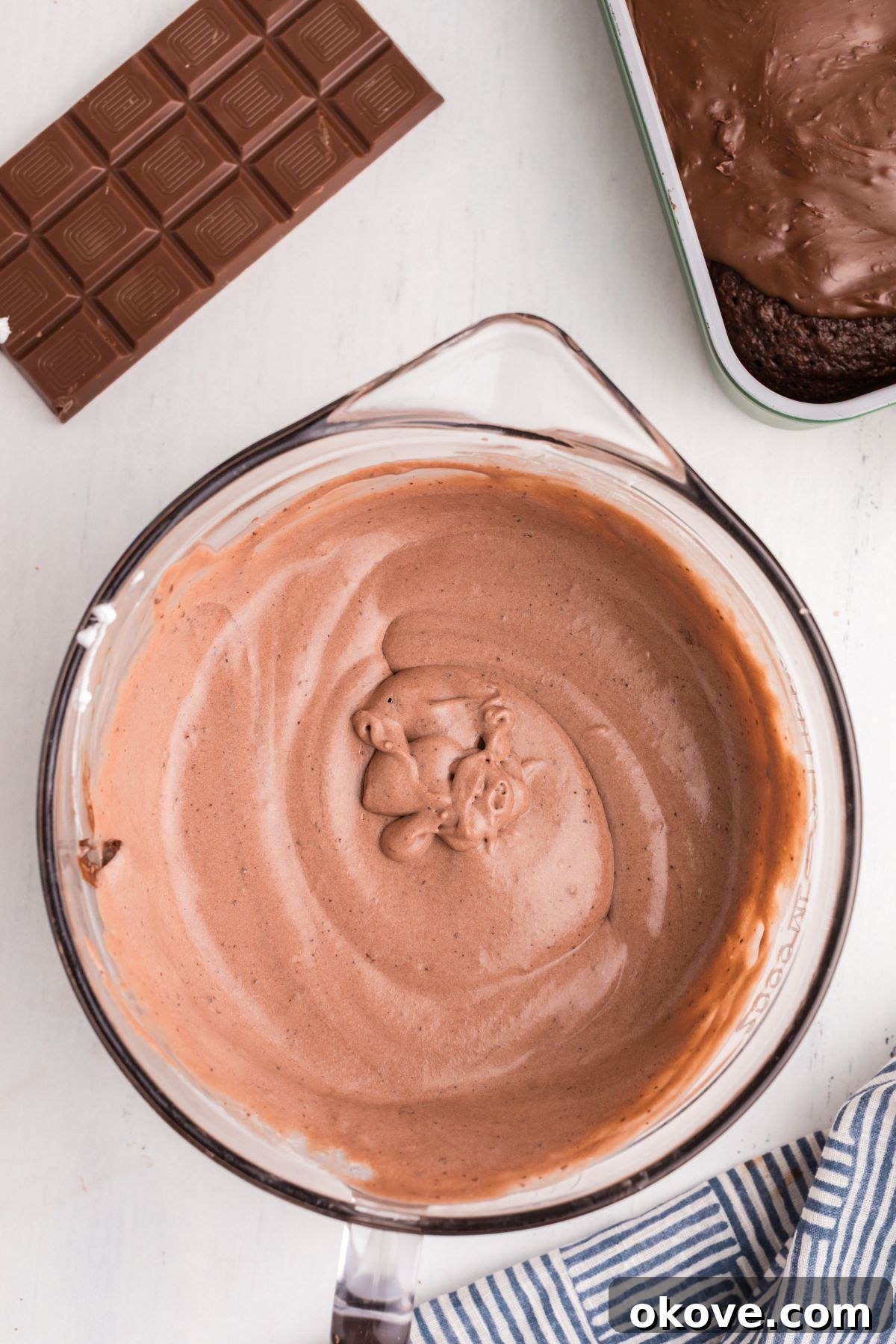 A clear glass bowl contains a creamy mixture of chocolate pudding and whipped cream, ready to be spread as a topping.