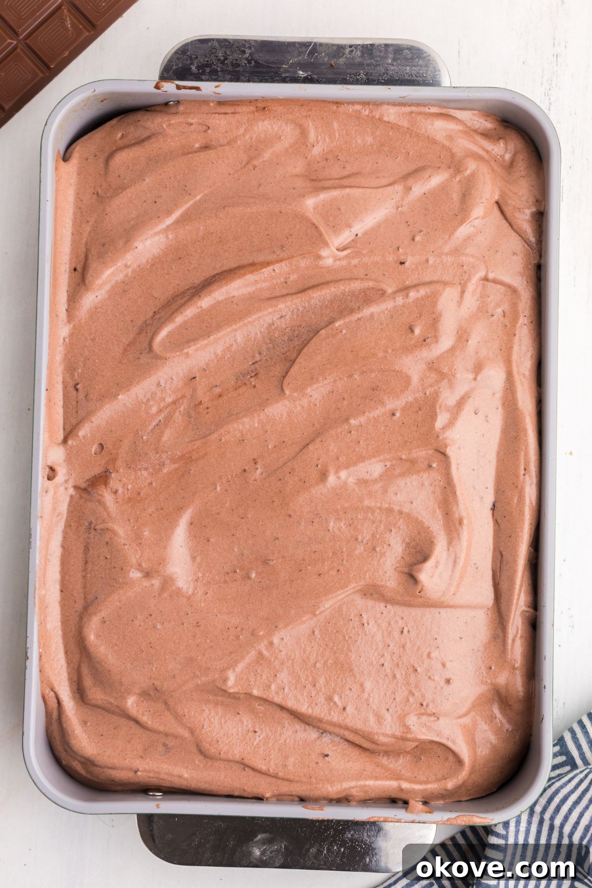 A fully frosted chocolate cake, topped with a smooth, even layer of chocolate whipped cream topping, ready for garnishing and chilling.
