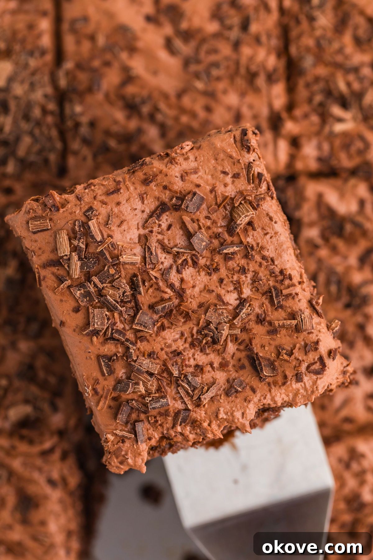 A perfect slice of chocolate poke cake, lifted gently by a spatula, showcasing its layers of moist cake, creamy filling, and topped with delicate chocolate shavings, ready to be served.