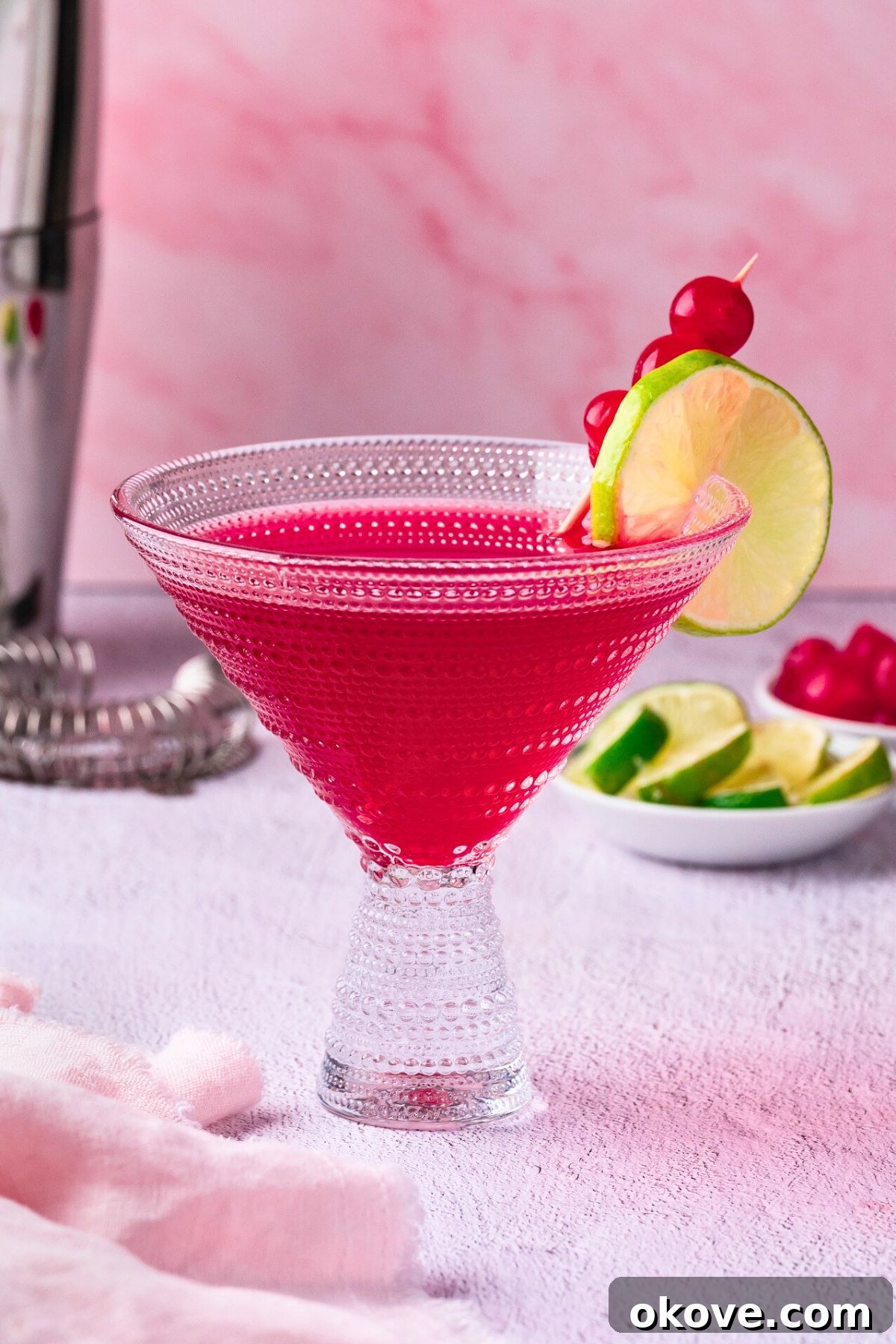 Pomegranate Martini Bliss 2 Vibrant ruby-red pomegranate martini in a chilled clear cocktail glass, garnished with a fresh lime wedge and a glistening maraschino cherry.