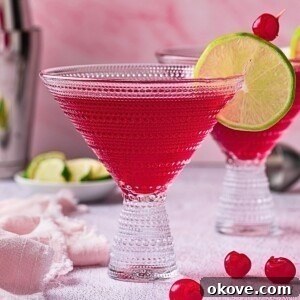 Pomegranate Martini Bliss 7 Red pomegranate martini in a clear cocktail glass with a lime wedge and cherry for a garnish.