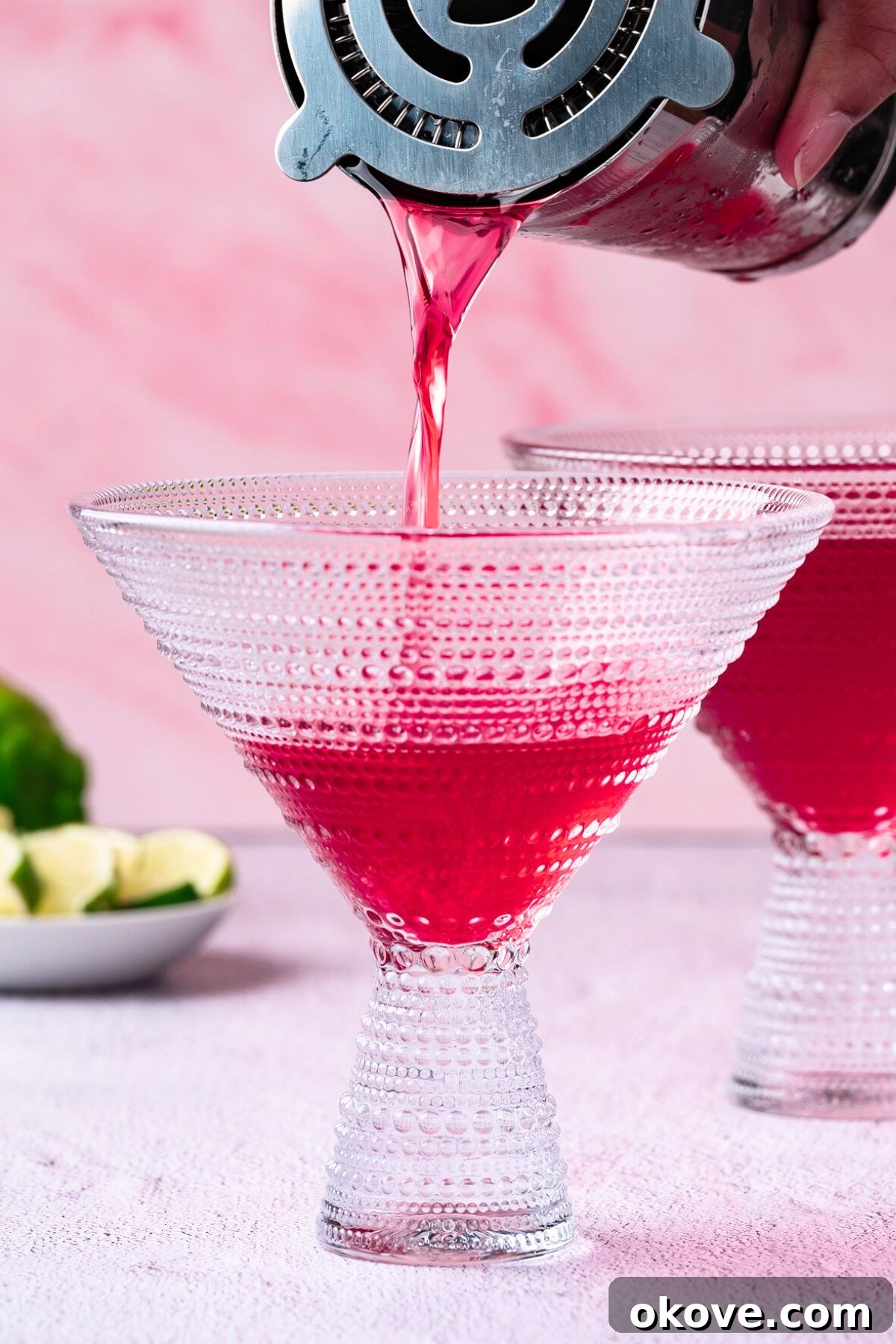Pomegranate Martini Bliss 5 A close-up shot of a vibrant red pomegranate martini being expertly strained from a cocktail mixer into a pristine, chilled martini glass, with ice being held back by the strainer.