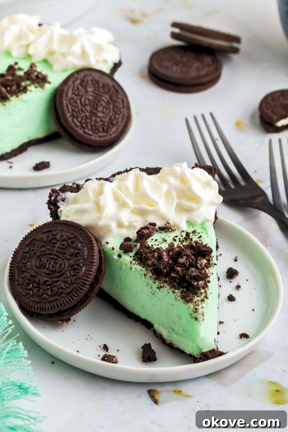 Minty Green Dream Pie 2 A perfectly sliced piece of creamy green Grasshopper Pie with a chocolate cookie crust, served on a small white plate, garnished with chocolate shavings.