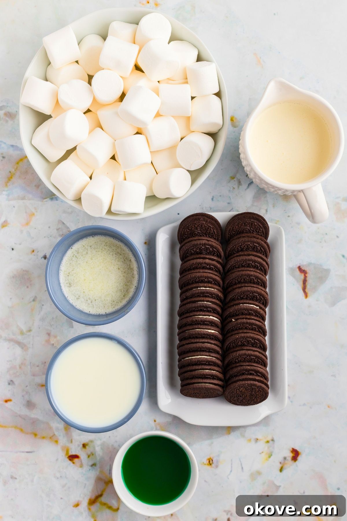 Minty Green Dream Pie 3 Various ingredients for Grasshopper Pie, including chocolate sandwich cookies, marshmallows, butter, and milk, meticulously measured and arranged in small dishes on a sophisticated marble countertop.