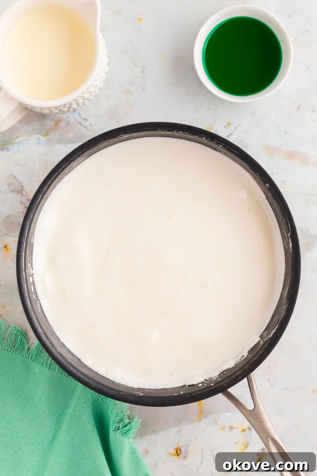 Minty Green Dream Pie 6 Melted marshmallows and milk or cream gently simmering in a stainless steel saucepan on a stovetop, forming a smooth, creamy liquid for the pie filling.