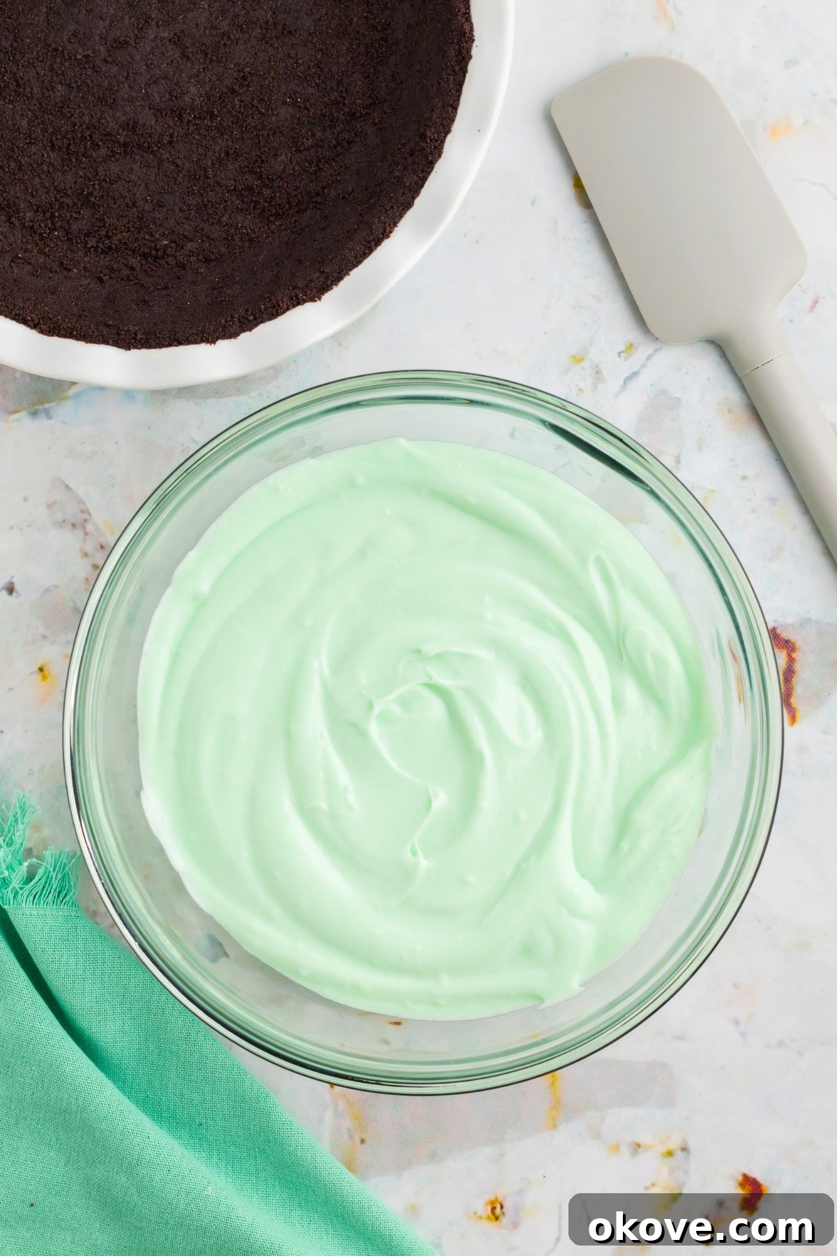 Minty Green Dream Pie 8 The smooth, green mint flavoring syrup being carefully mixed into the creamy marshmallow and whipped cream base in a glass bowl, creating the vibrant color of Grasshopper Pie.