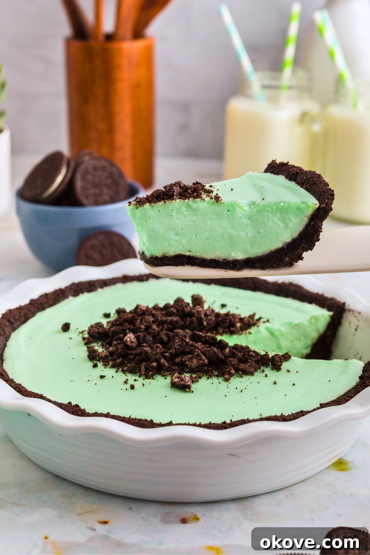 Minty Green Dream Pie 10 A serving of vibrant green Grasshopper Pie being carefully lifted out of a white pie dish with a spatula, revealing its rich chocolate cookie crust and creamy texture, ready to be enjoyed.