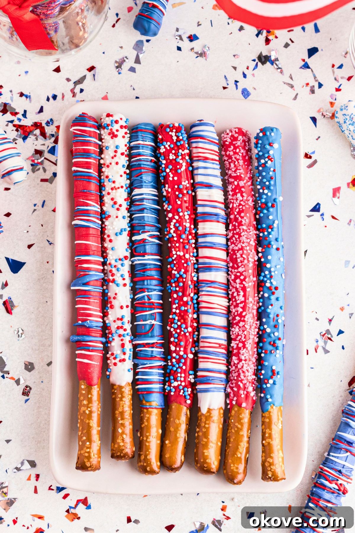 Dipped pretzel rods in red, white, and blue colors with sprinkles, arranged on a serving plate.