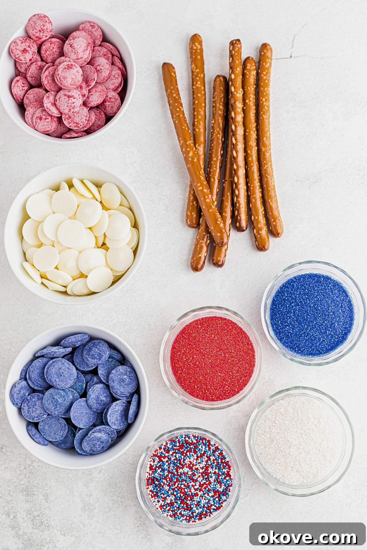Ingredients needed to make pretzels in patriotic colors, measured in small bowls on a marble table, ready for dipping.