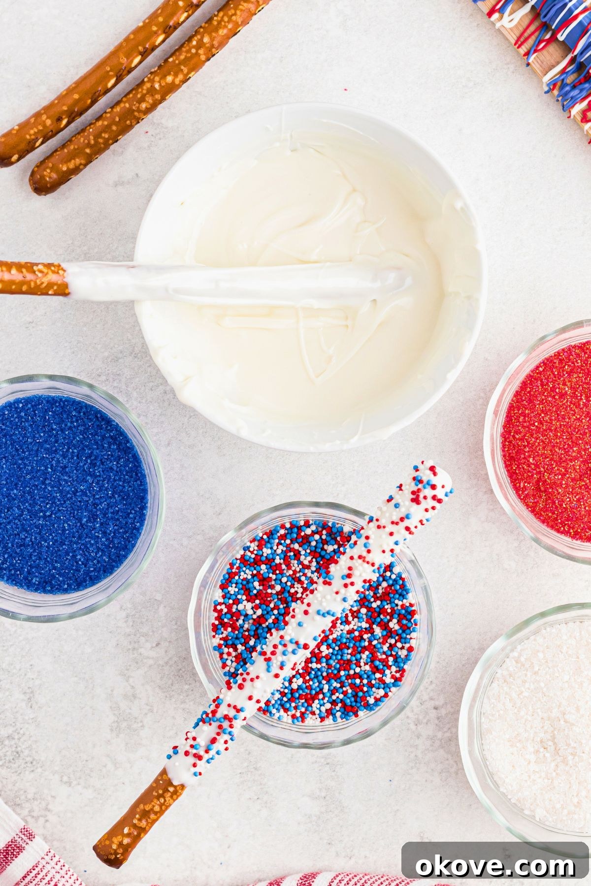 Pretzel rods resting in bowls of melting chocolates and candy sprinkles as they are dipped and decorated.
