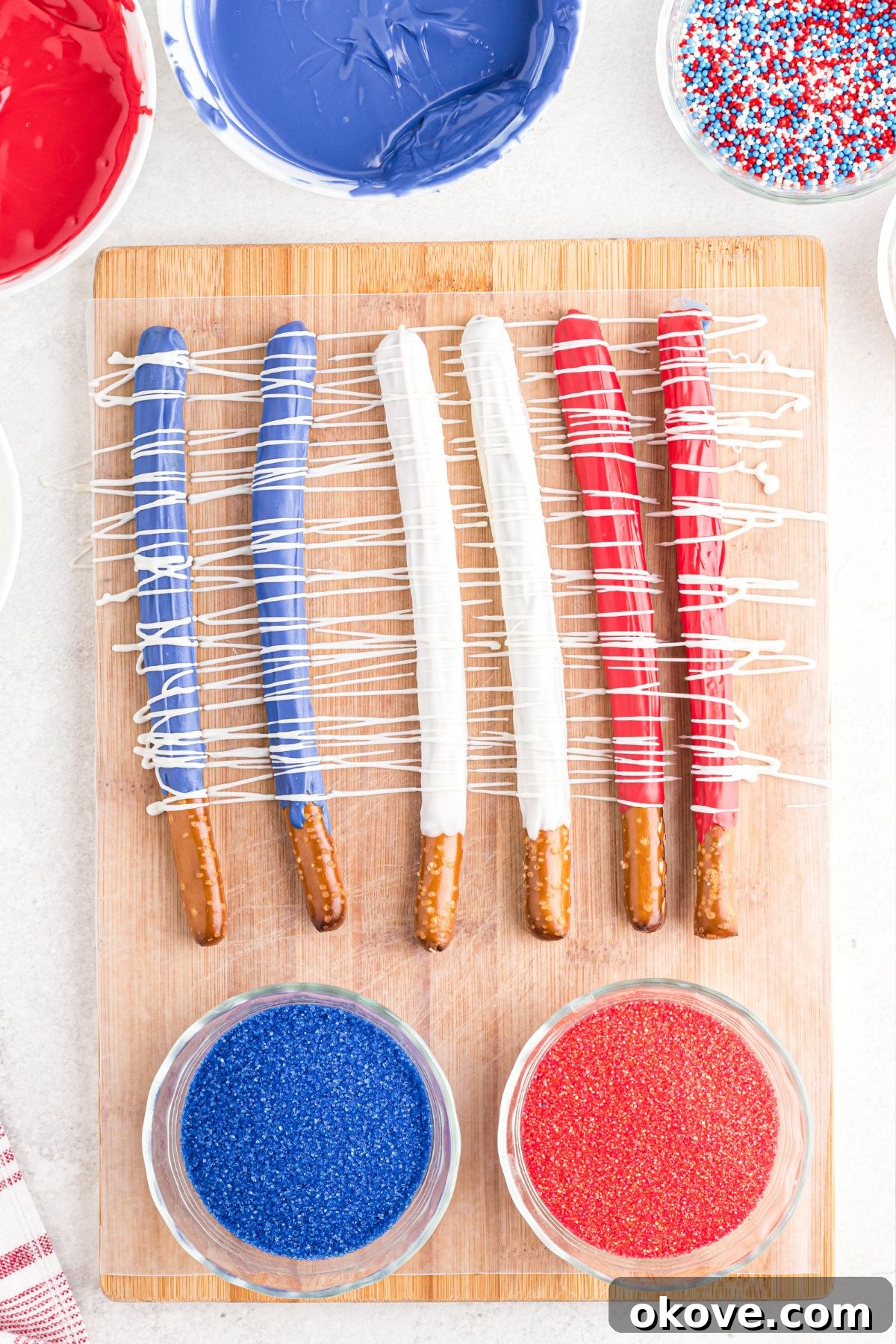 Pretzels dipped in candy melts then drizzled and topped with sprinkles, drying on wax paper.
