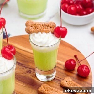 Green drink in a shot glass topped with cool whip and a red cherry.