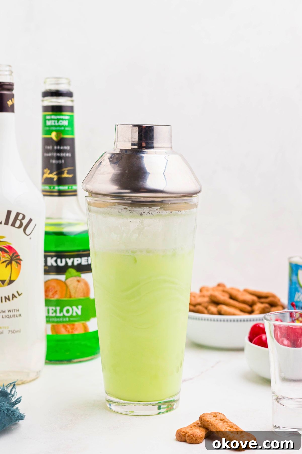 Green scooby snack shot mixture in a clear cocktail shaker on a white marble board. 