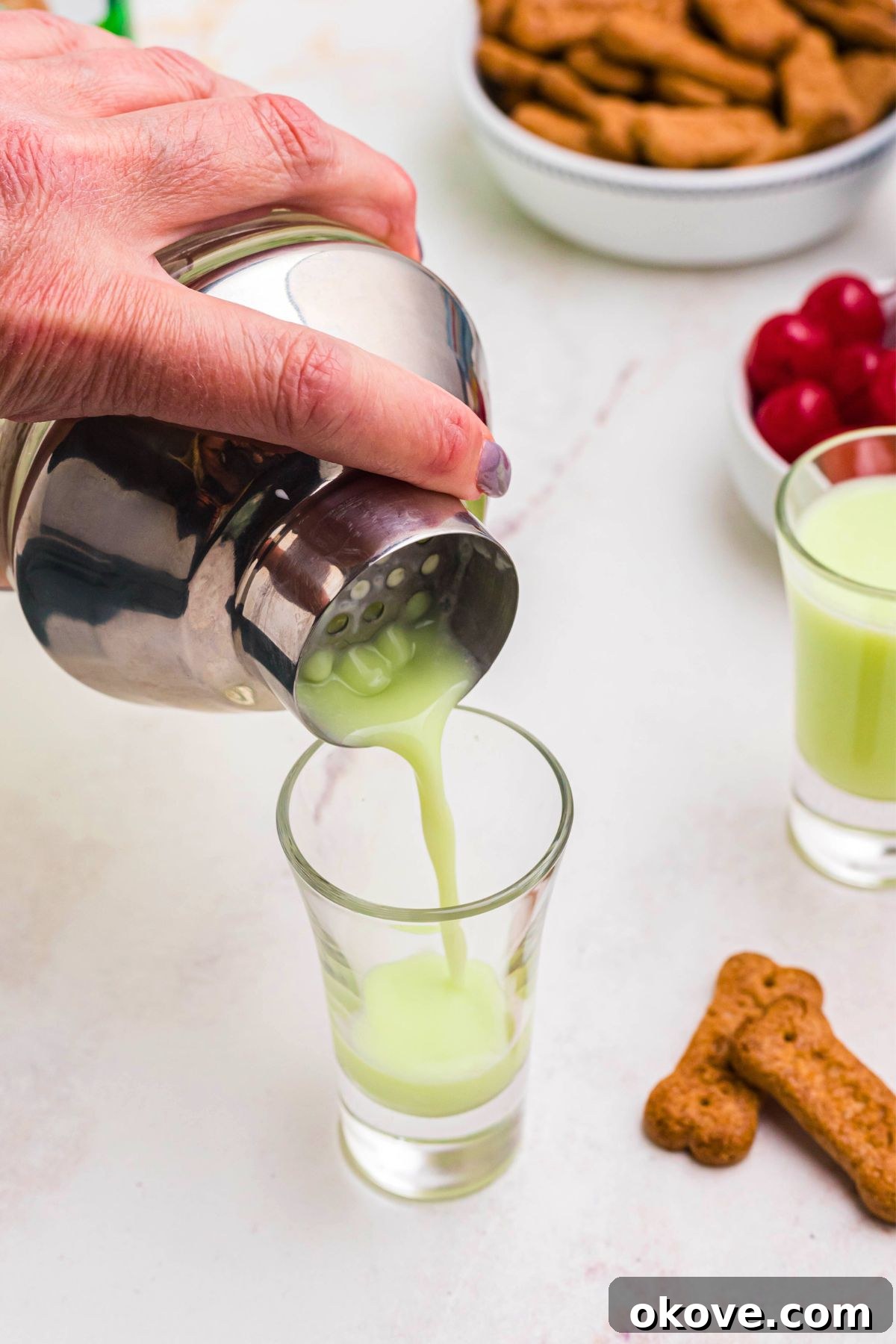 Green liquid cocktail ingredients being strained into shot glass. 