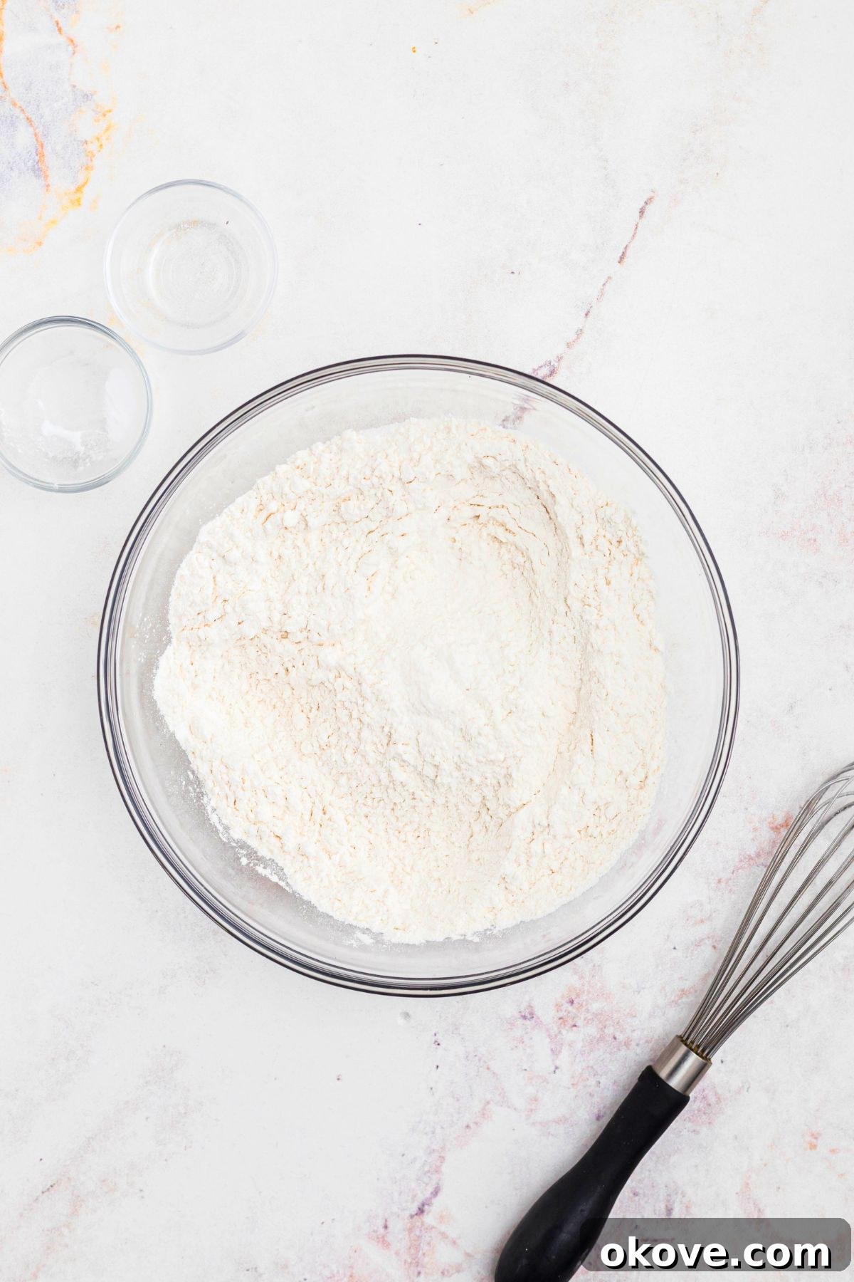 Flour and other essential dry ingredients expertly mixed in a clear glass bowl, ready for the next step of the cookie recipe.