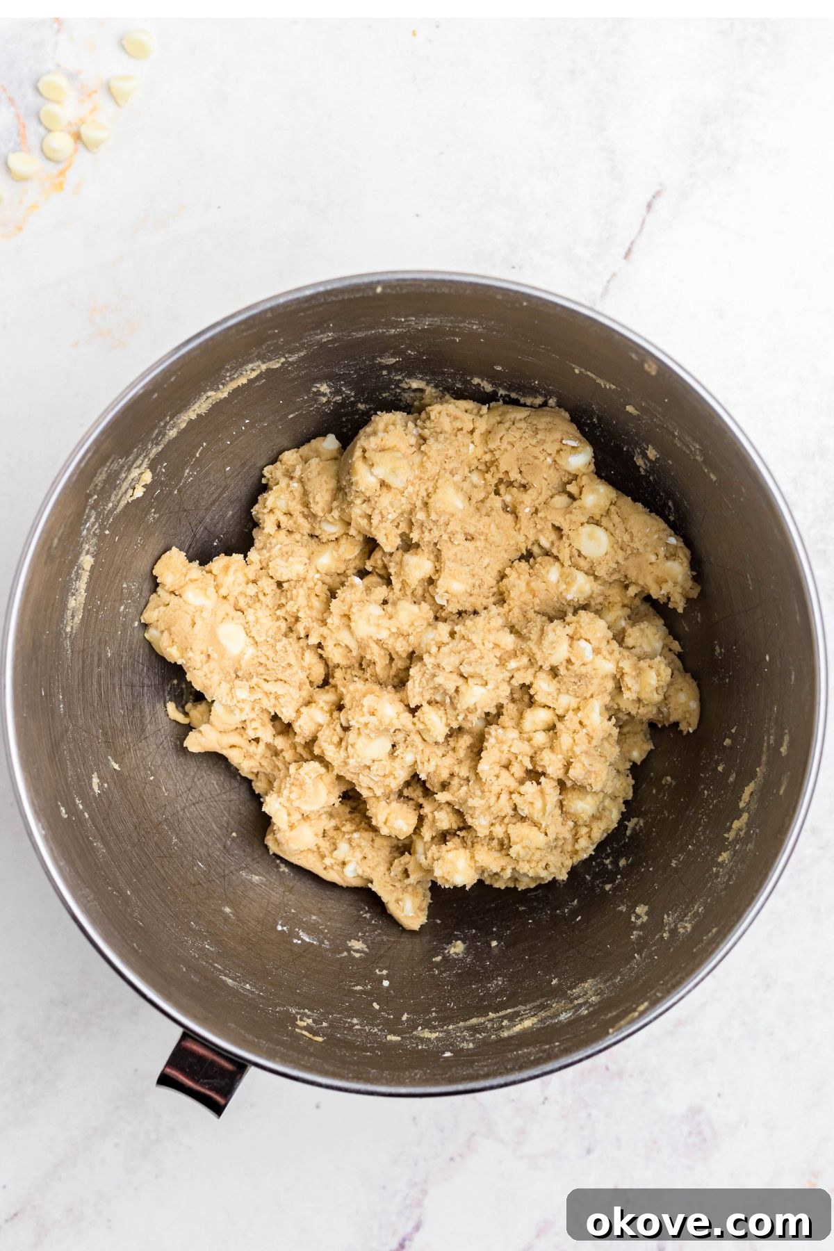 Soft cookie dough generously mixed with creamy white chocolate chips inside a large bowl, showcasing its readiness for baking.